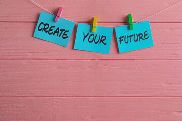 Paper notes with motivational phrase Create Your Future hanging on pink wooden wall. Space for text