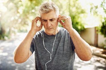 Fit, mature and healthy or sporty athlete resting after morning run, listening to music outdoors with earphones. Male jogger about to exercise or do cardio training workout for wellness lifestyle.