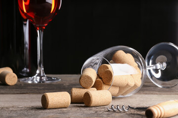 Glass with corks and corkscrew on wooden table