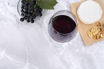 Glass of red wine and snacks served on white marble table, above view. Space for text