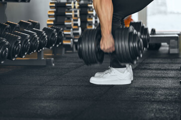 Muscular strong arms of an athlete lift dumbbells. Arms and dumbbells in motion and blurred, focus on running shoes and athlete's legs