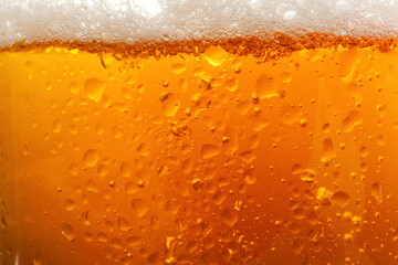 Glass of tasty cold beer with foam and condensation drops as background, closeup