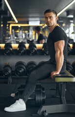 Fototapeta na wymiar Bodybuilder rests on a bench in the gym after a biceps muscle workout. Muscular Confident Athlete or Bodybuilder arms workout with heavy weights dumbbells