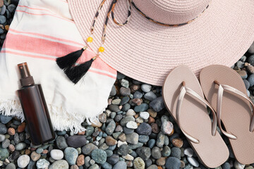 Beautiful hat, sunscreen and flip flops on pebbles, flat lay