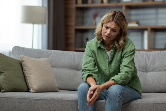 Sad senior mature woman sitting on sofa in living room wife grieving divorce depressed.