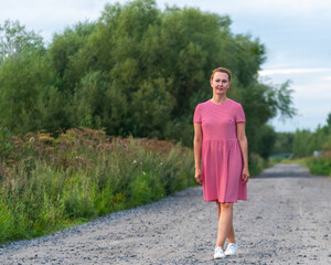 a woman in a red dress walks along a country road on a summer evening