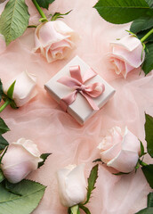 Top view of pink roses and gift box on pink tulle background.
