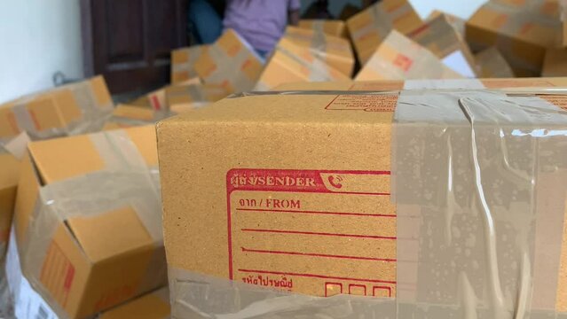Close up cardboard box package with sender and postcode word screen on parcel with blurred person working in background