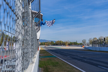 Man holding and waving checkered race flag at the finish line on a race track. Victory, achievement, success and sport concept.