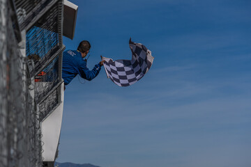 Man holding and waving checkered race flag at the finish line on a race track. Victory,...