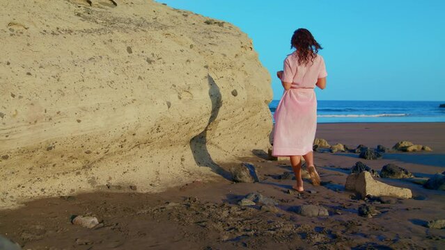 A female on a deserted beach undresses and prepares to swim. Woman in a bathing suit goes swimming, on vacation by the ocean.
The woman goes for a swim. Red swimsuit and summer dress by the ocean. 