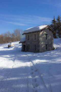 Italian mountain winter landscape. Small stone house in the woods. Shadow play in the snow. Combai, Italy. Vertical image