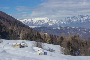 Postcard panoramic landscape. Small stone houses amid snowdrifts with mountains in the background. Photographed in Combai, Treviso, Italy.