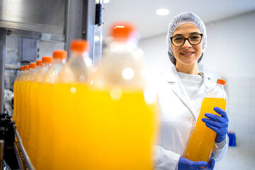 Food factory female supervisor standing in bottling plant and holding orange juice bottle. - Powered by Adobe