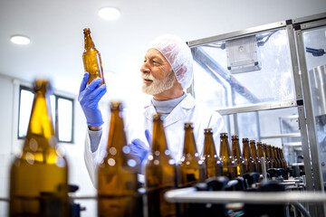 Experienced factory worker controlling beer bottle production in beverage plant.
