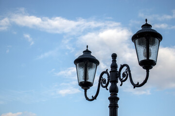 Openwork street lamps against the blue sky during the day. The outlines of ornate lighting...