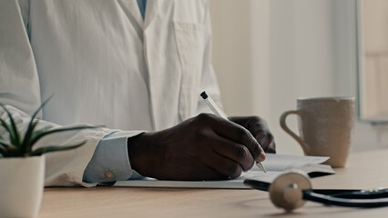 Unrecognizable man doctor therapist cardiologist wears medical coat sit at desk write diagnose in notebook planning work day prescribe medicine results prescription writing professional recommendation