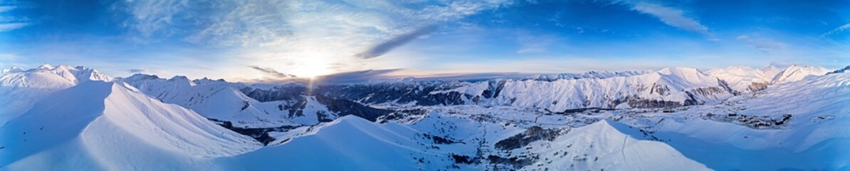 Fototapeta na wymiar Wide aerial panorama of snowy mountain ridge on winter sunrise. Stunning mountains range covered with snow powder on ski resort at sunset. Caucasus mountain peaks skyline in Georgia - Gudauri.