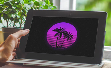 Hand holding tablet with retwowave style purple logo with palm trees on the screen