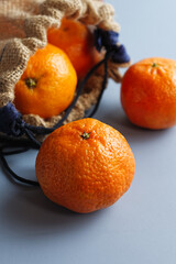 Close up of tangerines in a jute bag, on a blue background.