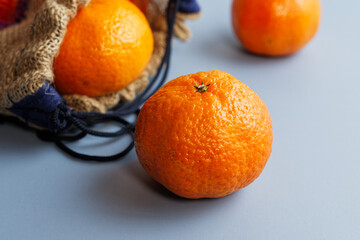 Close up of tangerines in a jute bag, on a blue background.