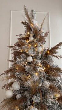 Christmas Tree view from top to bottom. Hall room with a fireplace with candles and gifts under designer snow tree with lights and balls in beige, gold and white colors. Vertical video