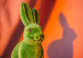 Green cute funny Easter bunny with long ears on the orange sunny background in springtime. Easter holiday in April. Toy decorative dreamy hare - a symbol of Easter. Smiling rabbit portrait close-up