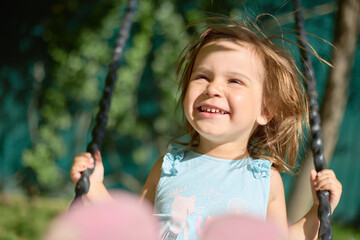 A child on a swing is playing on an outdoor playground. An active child is swinging on a swing. Healthy summer activity for children. A little girl in the fresh air..