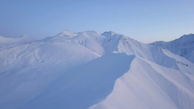 Aerial of snowy mountain slopes full of powder for freeride at ski resort on winter sunrise. Mountains range of backcountry covered with virgin snow. Caucasus peaks skyline with twilight afterglow.
