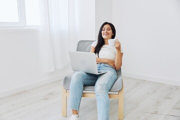 Woman relaxing at home sitting in a chair and watching a movie on her laptop with a cup of tea, happiness and laughter comedy, freelancer lifestyle