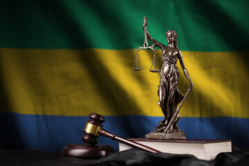 Gabon flag with statue of lady justice, constitution and judge hammer on black drapery. Concept of...