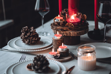 Rustic table decor for Christmas or New Year family dinner. Centrepiece with red candle, dry orange, cone, cinnamon, anise. Zero waste eco-friendly home. Cozy atmosphere, dark background. Close up