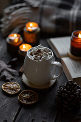 Autumn cozy home composition with hot chocolate with marshmallow and candles. Aromatherapy on a grey fall morning, atmosphere of cosiness and relax. Wooden background, books, close up.