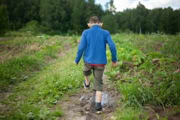 Child walks in mud. Boy trampling on puddle. Schoolboy plays with water. Blue blouse.