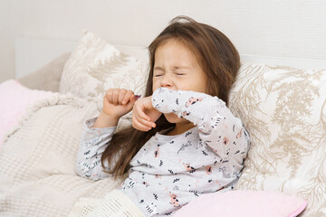 Exhausted little long haired brunette girl yawning or sneezing with close eyes, covering mouth with...
