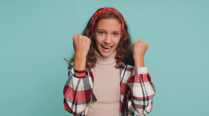 Young teenager child girl kid shouting, raising fists in gesture I did it, celebrating success, winning, birthday, lottery jackpot goal achievemen. Preteen children isolated on blue studio background