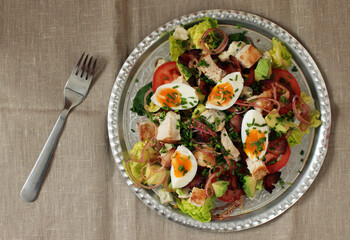 Cobb salad with chicken, avocado, tomatoes, eggs, bacon and cheese with sauce on a table, top view