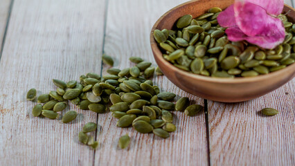 Pipas de calabaza naturales sobre mesa madera blanca y en un cuenco de madera redondo