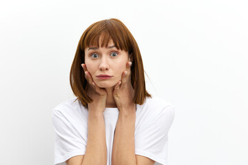 Fototapeta premium a funny, emotional woman stands on a white background in a white T-shirt and holds it with her hands while making a funny face. Horizontal photo with an empty space for inserting an advertising layout