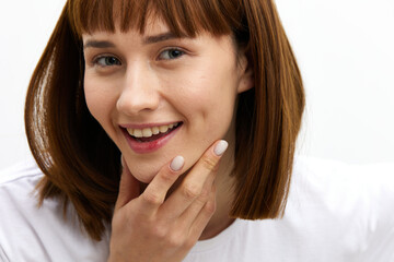 a sweet, happy woman smiles pleasantly looking at the camera standing in a white T-shirt on a light background Horizontal photo with an empty space for inserting an advertising layout
