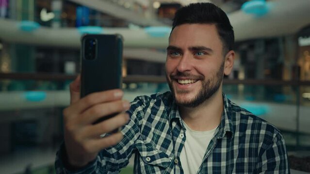 Smiling arabian caucasian male blogger businessman look at mobile phone camera talk video call in shopping mall happy young man chatting online recording blog use modern tech for remote communication