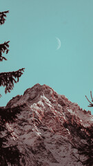 Moon in daylight over snowy mountaintop