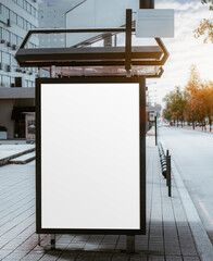 Blank vertical ad mockup in a bus terminal for commercial use, next to a residential building and with the afternoon sun flare hidden by the clouds; empty advert placeholder template on the bus stop