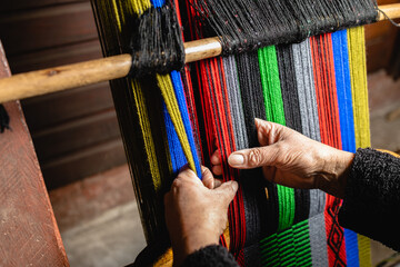 Unrecognizable elder woman's hands using a homemade craft loom to weave colorful wool