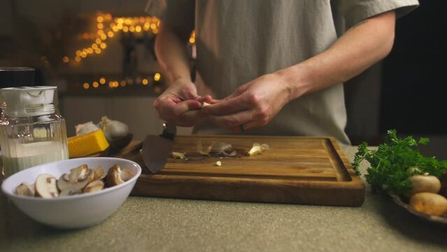 Video. A young man prepares a delicious holiday dinner. Peels garlic on a cutting board. In a bowl, peeled mushrooms, milk in a jug, cheese, herbs. Simple and delicious recipes for the whole family.