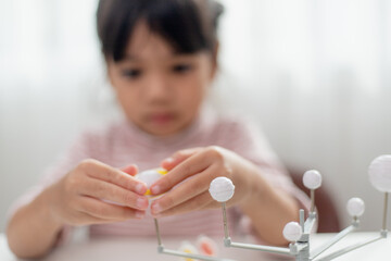 Asian Little girl studies the solar system in geography class. looking at the scale model of planets