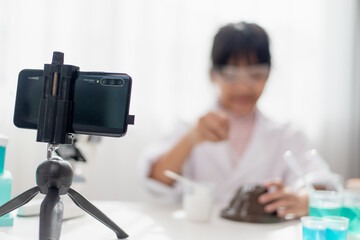 Asian school girl making easy chemistry experiments and recording a video for his followers, Young blogger kid posing in front of camera for vlog, Children make vlog for social media channel concept.