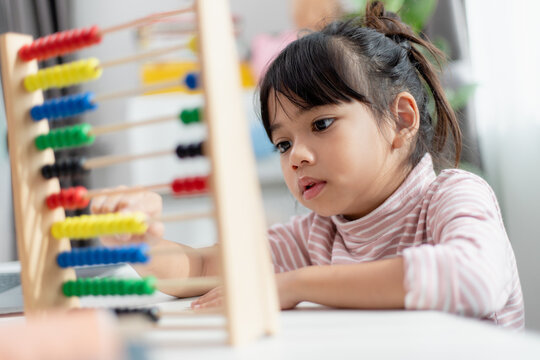 A young cute Asian girl is using the abacus with colored beads to learn how to count at home