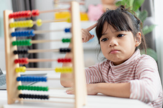A young cute Asian girl is using the abacus with colored beads to learn how to count at home
