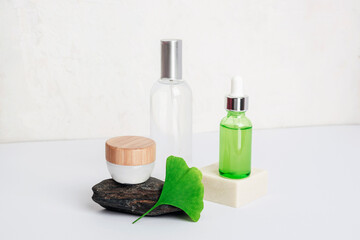 Fototapeta na wymiar Fresh green ginkgo biloba leaf, cosmetic serum and tonic bottles, cream jar on white table. Natural cosmetics concept. Closeup
